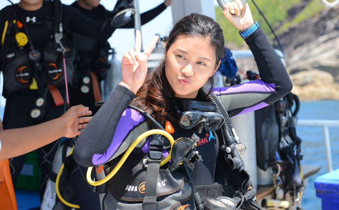 young asian female diver gives peace sign before diving in
